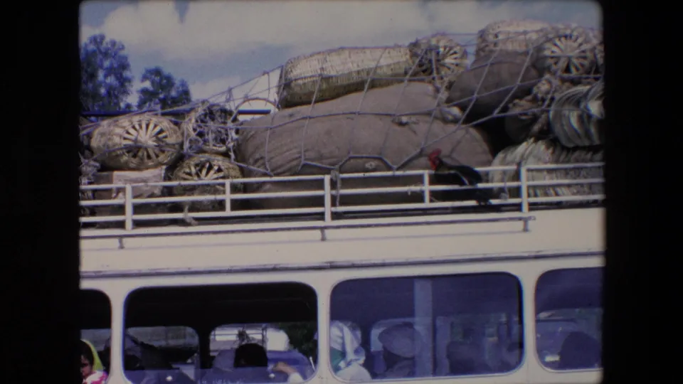 The 8mm frame shows tied sacks and baskets stacked on a bus roof in Algeria, with passenger silhouettes and faces visible through the windows.