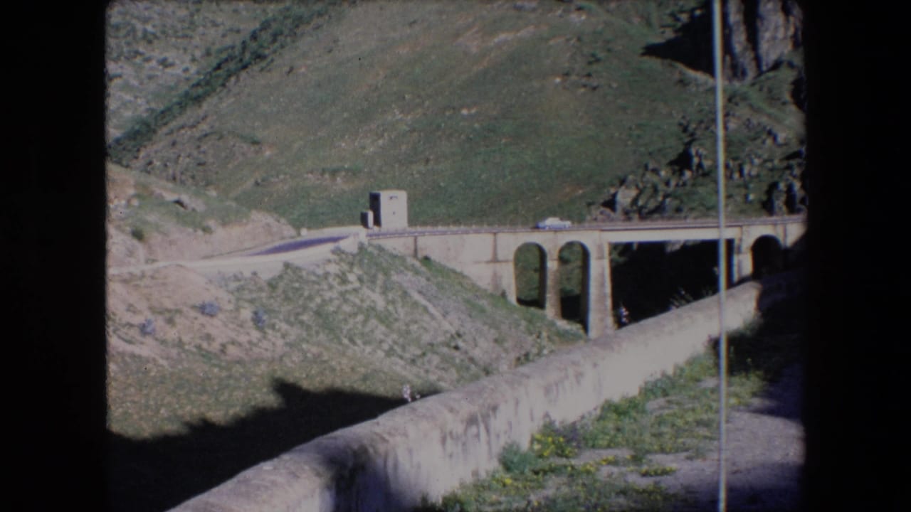 Car traveling across a bridge set into a green mountain slope.