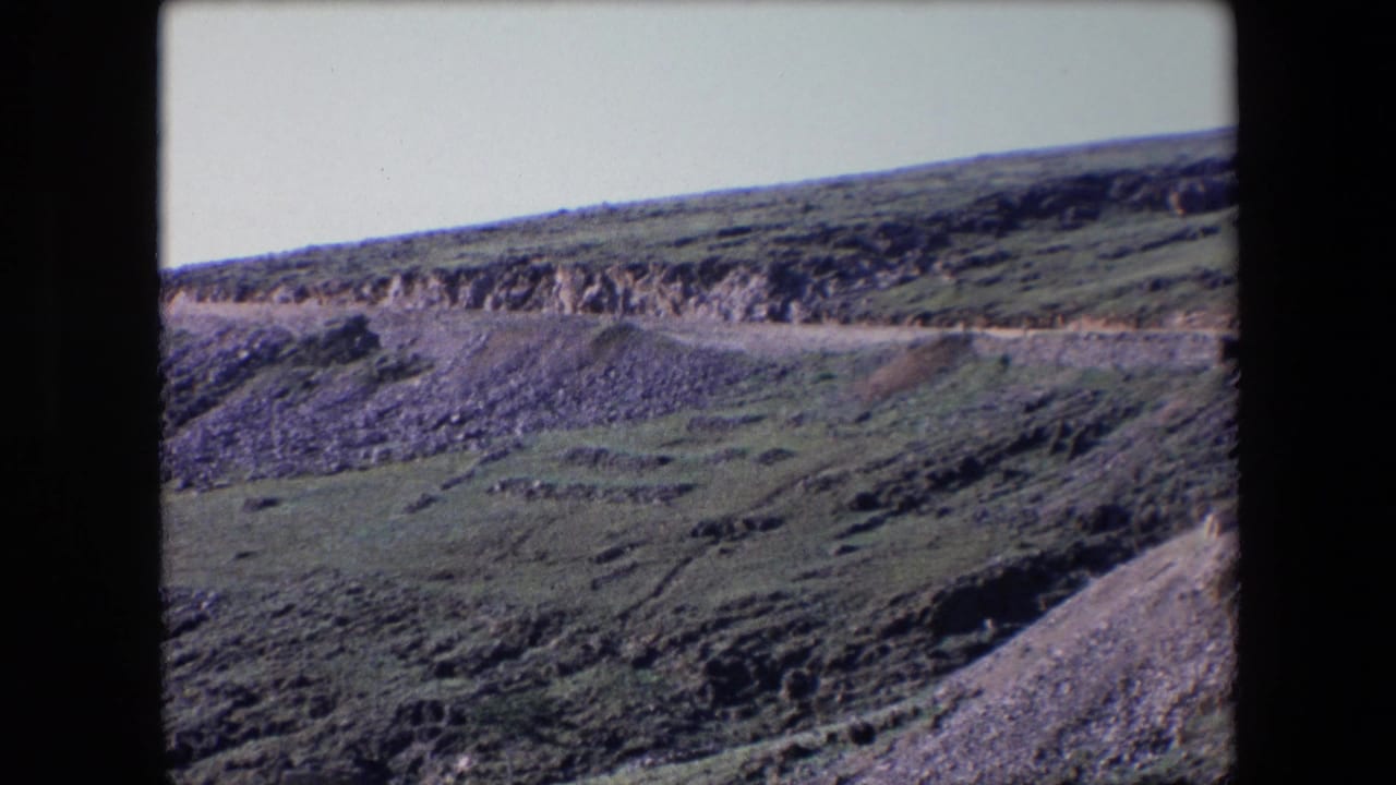 Winding road and rocky hillside viewed from across the slope.