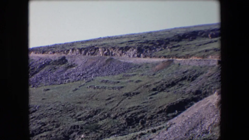 1971 Algeria travel frame with a curving road traversing exposed rock and sparse vegetation on a steep hillside.