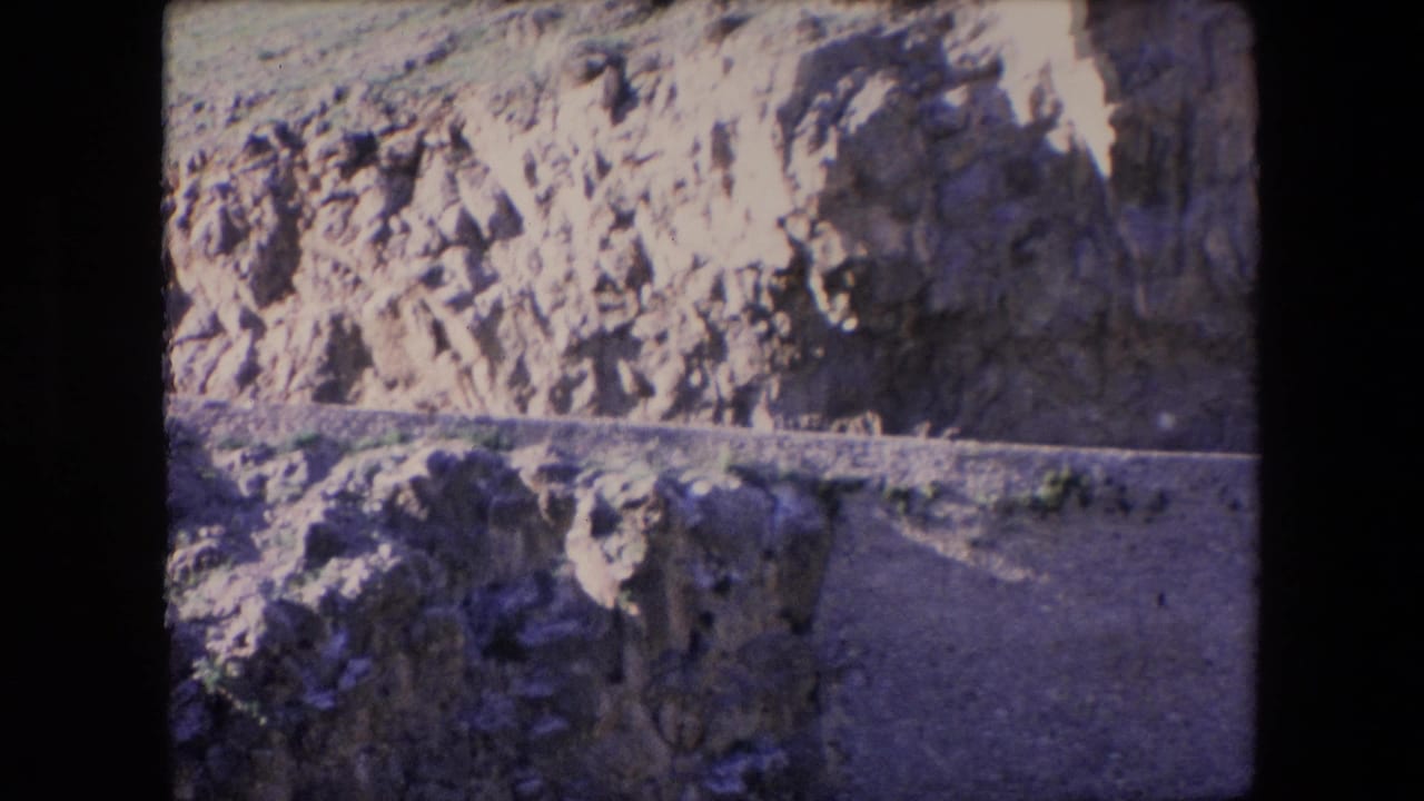 1971 Algeria 8mm frame showing a sunlit rocky hillside, exposed earth, shadowed stone faces, and a narrow dirt track across the terrain.