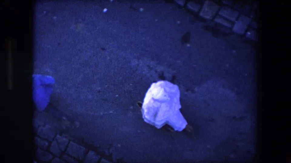 A high-angle 1971 Algeria frame shows the white sheet-covered person on the pavement while another passerby in blue appears along the left edge.