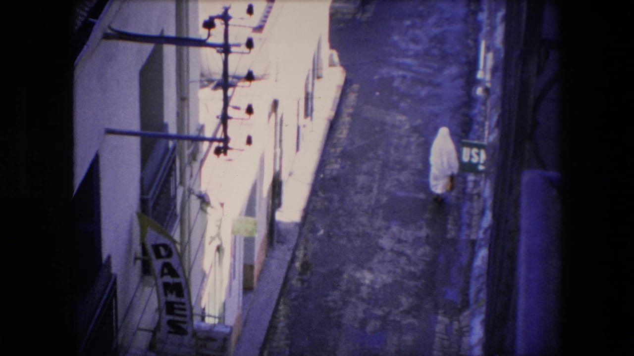 Nun in a white habit walking down a narrow alley seen from above.