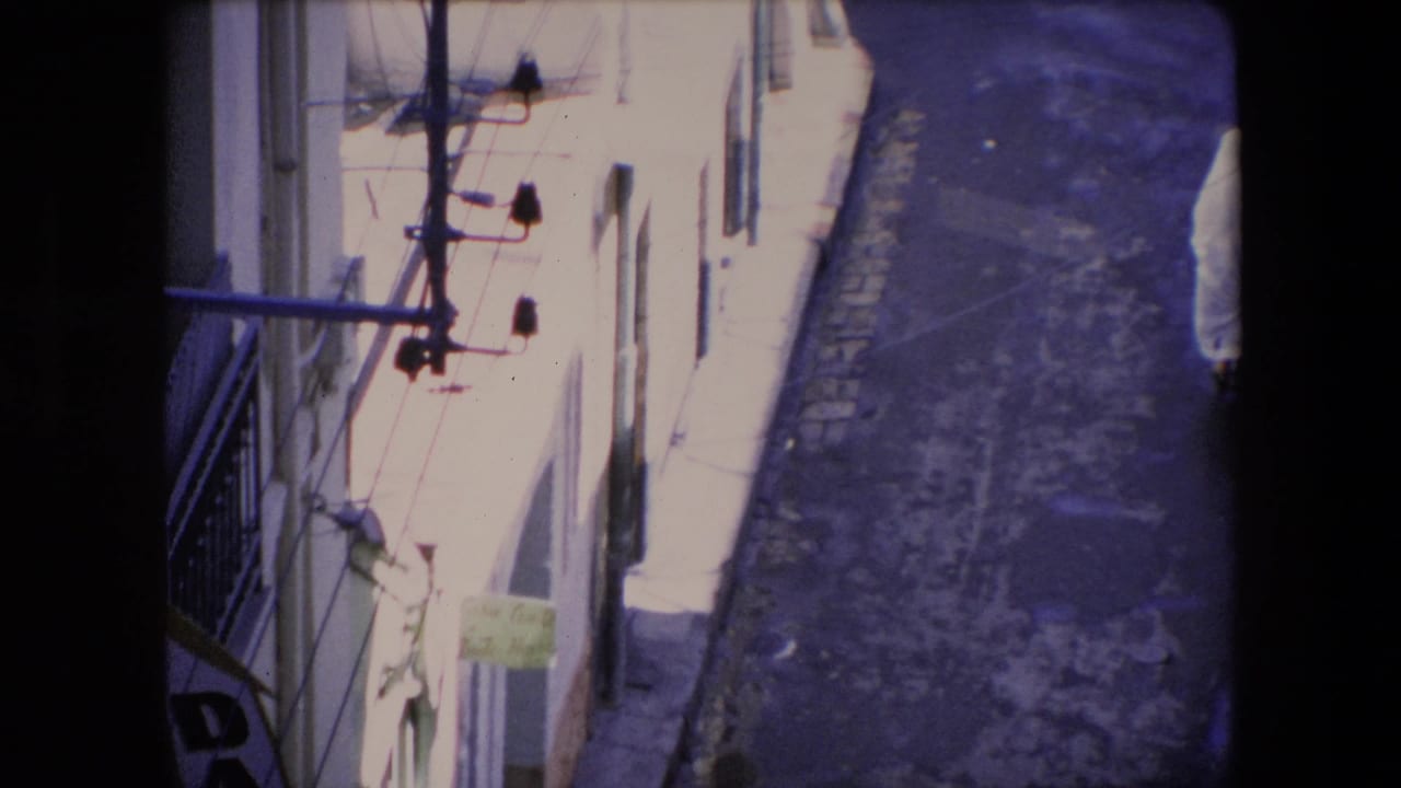 Narrow sunlit alley with white building walls, utility fixtures, and partial signage.