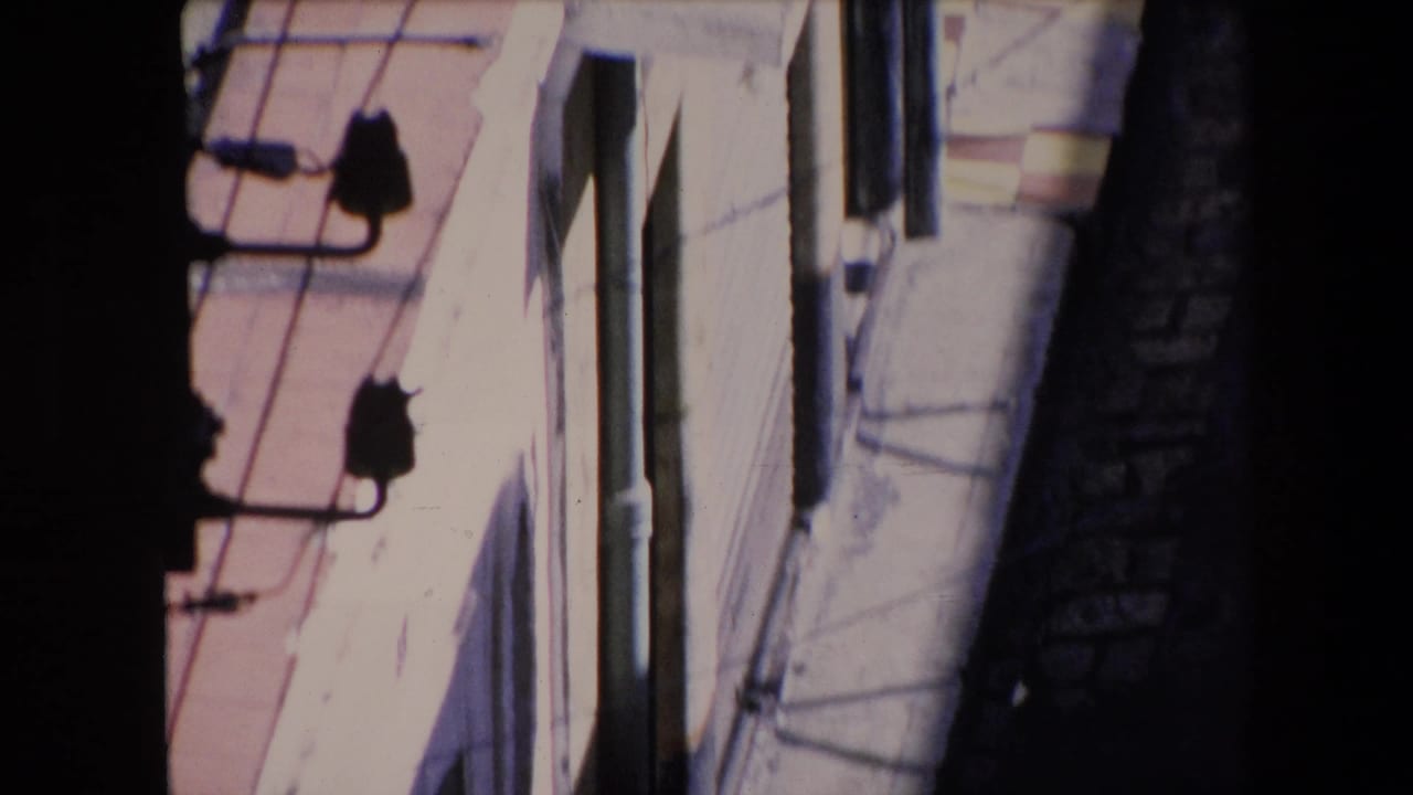 High-angle view of pale building walls, rooftop edges, wires, and a dark narrow alley below.