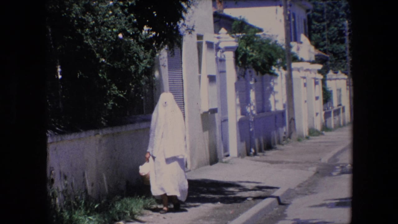 Woman in white covering approaches the camera on a quiet street with a basket in one hand.
