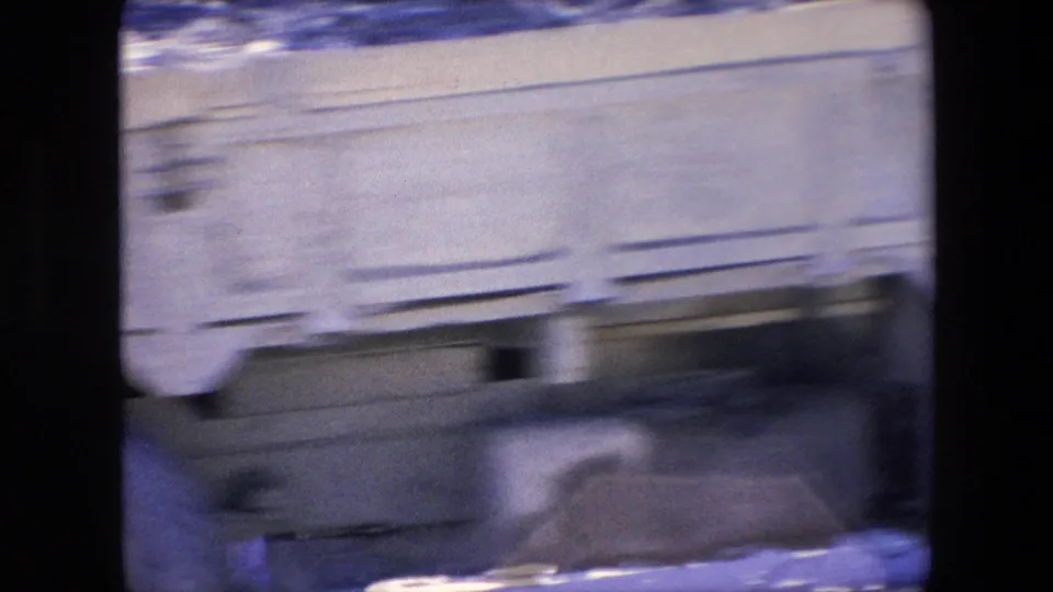 A light-colored vehicle passes in motion blur across the foreground while the Algerian street market remains partly visible behind it.