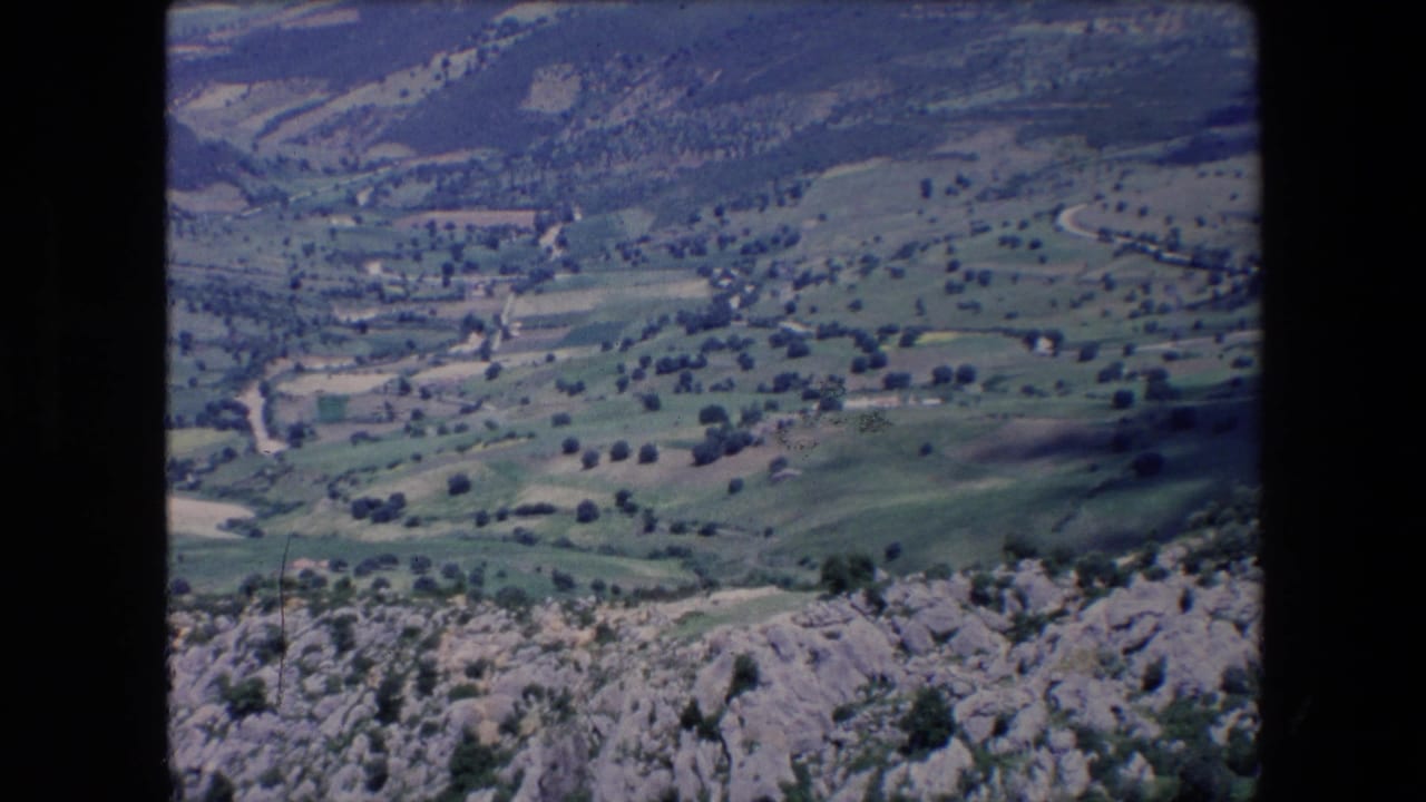 Green hills and a winding valley road seen beyond a rocky ledge.