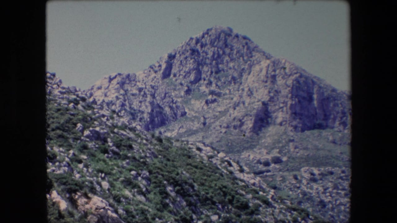 Rocky mountain peak with sparse greenery under a bright sky.