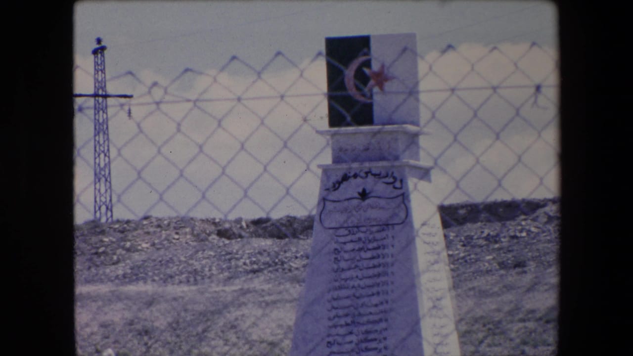 Crescent-and-star plaque above a white monument behind chain-link fencing.