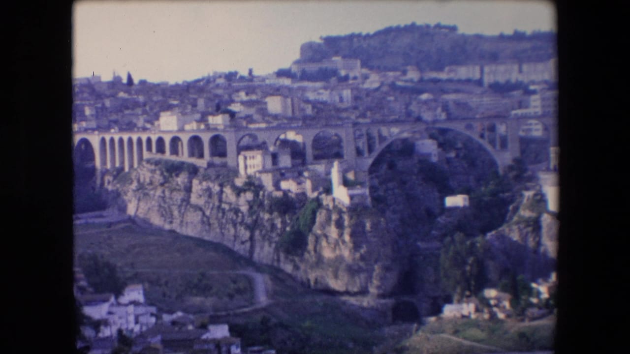 Distant cityscape with a large bridge spanning cliffs and buildings spread across the hillside.