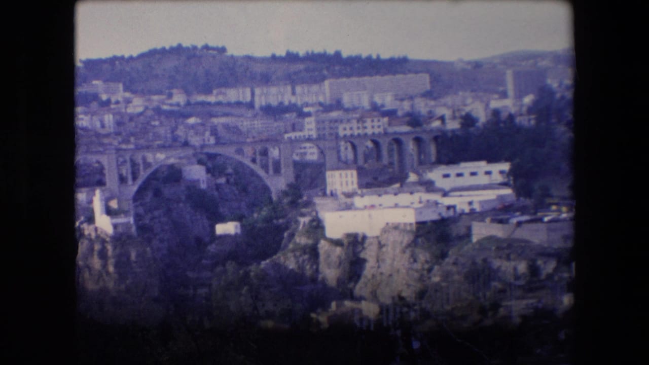 1971 Algeria 8mm frame showing an elevated city overlook with a prominent arched bridge, dense hillside buildings, and dark film borders.