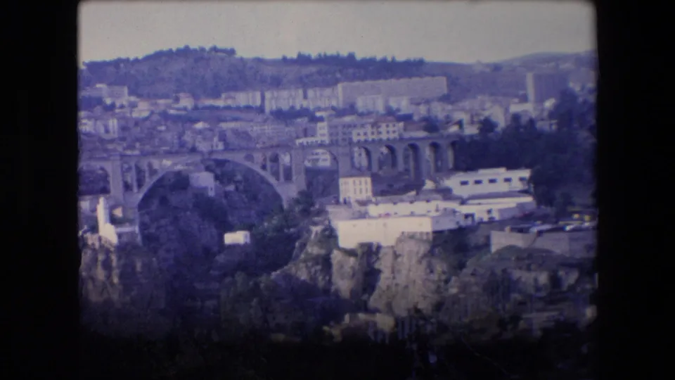 1971 Algeria 8mm frame showing an elevated city overlook with a prominent arched bridge, dense hillside buildings, and dark film borders.