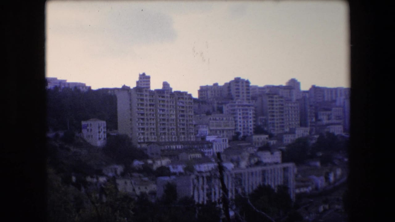 Hillside cityscape with tall apartment blocks and lower buildings below.
