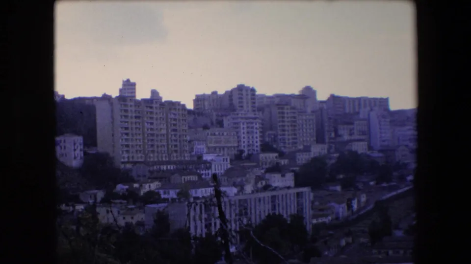 1971 Algeria 8mm frame showing a wide elevated view across apartment towers, lower hillside buildings, and a route through the lower right foreground.
