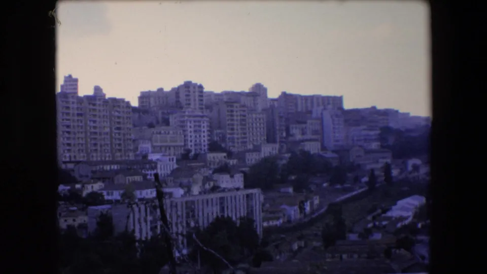 1971 Algeria 8mm frame showing a static elevated city panorama with dense apartment blocks, smaller hillside buildings, and a corridor running through the lower frame.