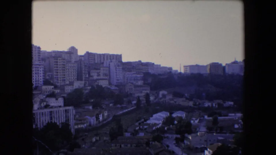 Vintage 8mm frame from Algeria in 1971 showing a broad elevated view over apartments, lower residential buildings, tree cover, and possible roads on a hillside.