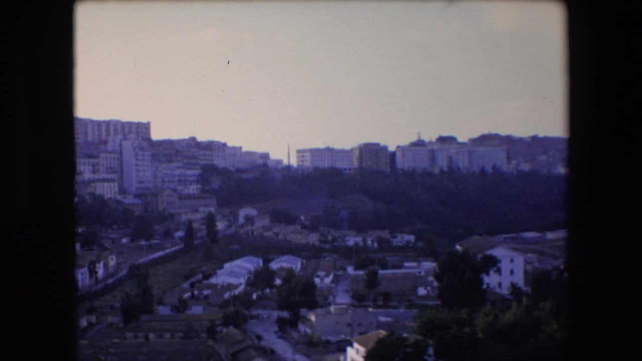 1971 8mm travel footage shows a distant North African hillside city view with dense buildings, tree cover, and soft purple-blue film color.
