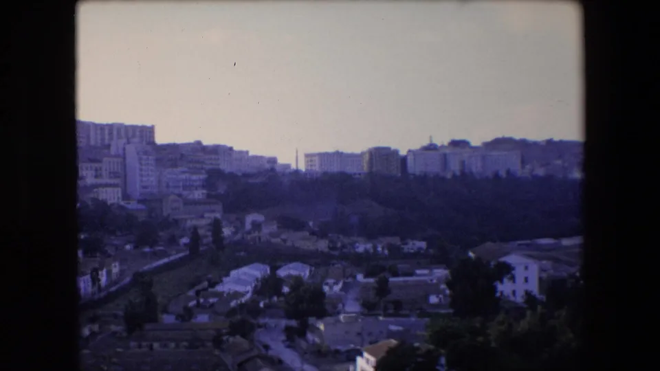 1971 8mm travel footage shows a distant North African hillside city view with dense buildings, tree cover, and soft purple-blue film color.