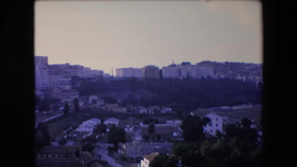 A distant urban hillside landscape appears in the 1971 home-movie footage, with apartment blocks, greenery, and a soft aged-film color cast.