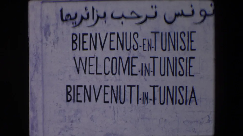 1971 Algeria travel footage showing a weathered welcome sign for Tunisie with Arabic script above French, English, and Italian lines.