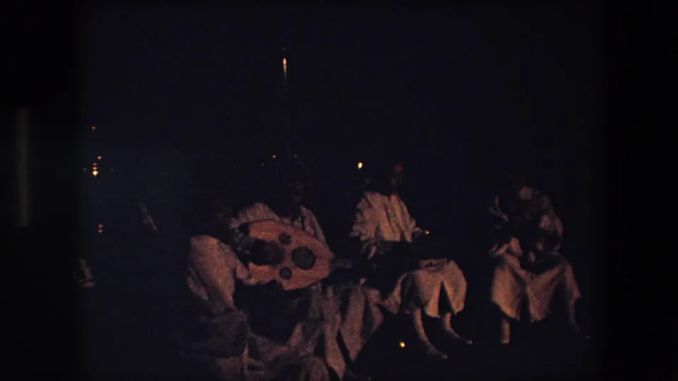 A dark, grainy final frame from the same 1971 home movie appears to show people gathered outdoors at night, with faint lights behind them and clothing details only partly visible.