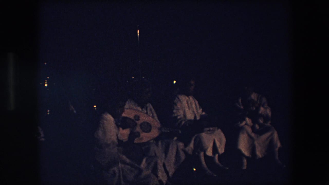 In the 1971 Algeria footage, the group remains seated in a dark outdoor setting while one performer holds a large round lute-like instrument and others sit nearby.