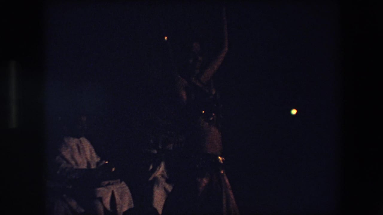 Dark performance scene with a dancer at right and a seated musician partly visible at left.