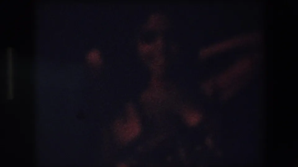 Dark 1971 Algeria 8mm frame with the dancer blurred in motion, showing warm reflections from the costume against a nearly black background.