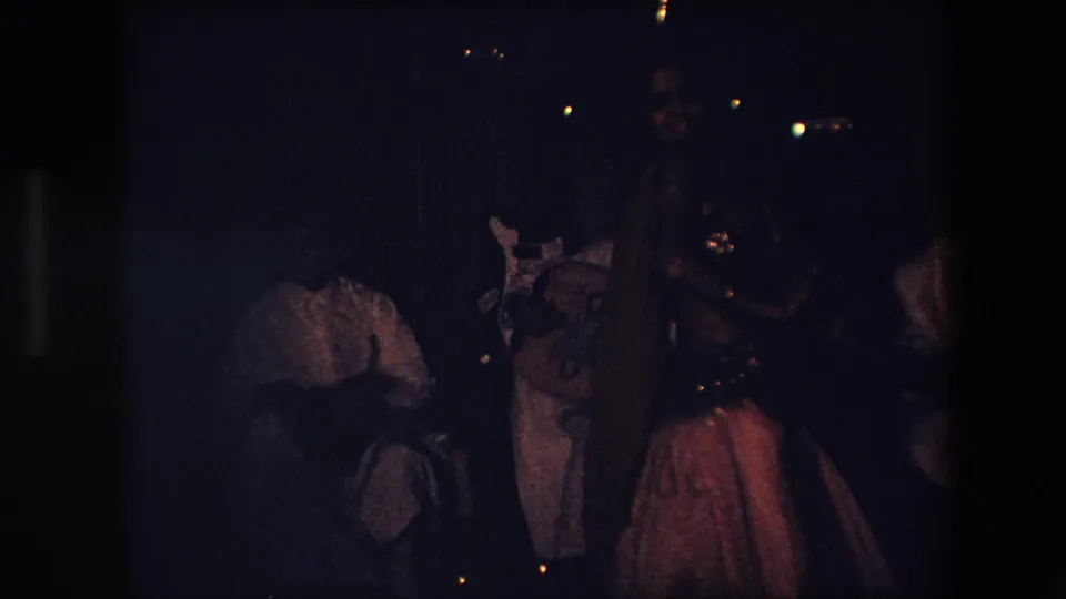 A dark 1971 Algeria frame shows the dancer near the right side of the venue, with background figures and faint lights visible behind her.