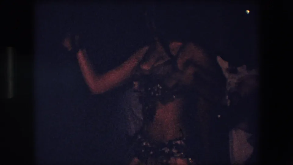 The final frame shows the dancer in side view with an extended arm, her costume and skirt partly lit while another person remains indistinct at the edge of the dark room.
