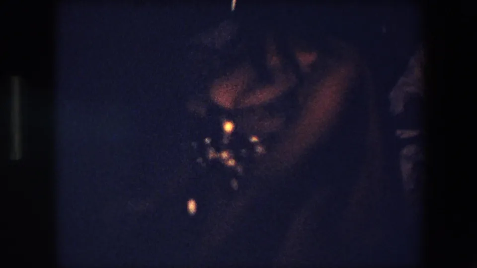 The handheld 8mm camera catches a close, underexposed view of the belly dancer's face and sequined costume during the 1971 Algeria performance.