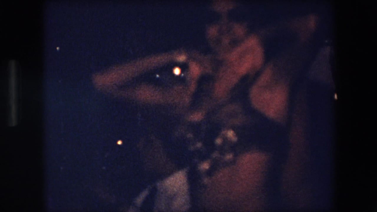 In 1971 Algeria 8mm footage, a belly dancer in a beaded costume performs under dark, low-light conditions near a musician.