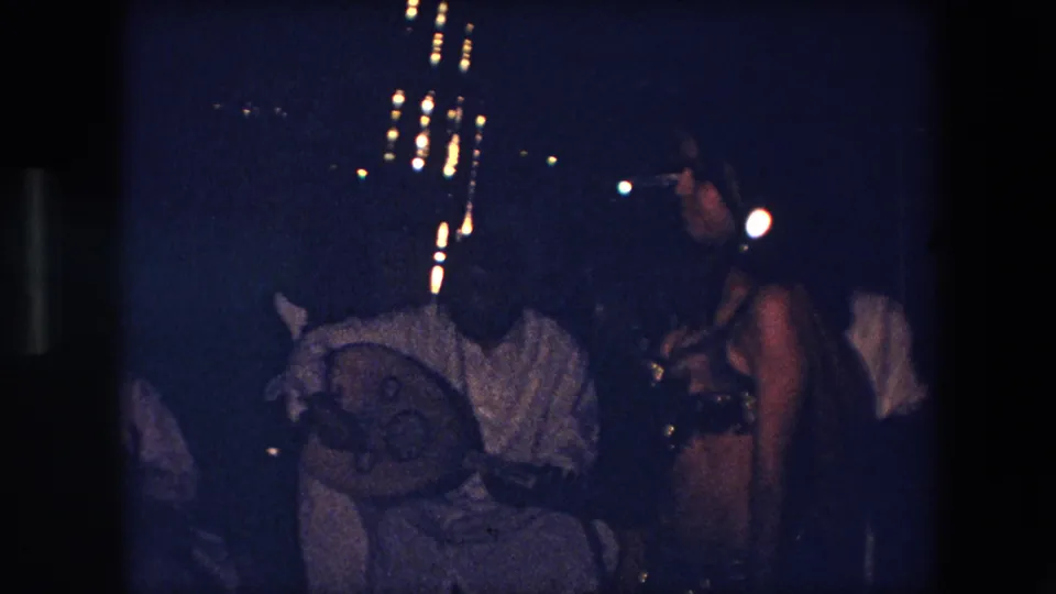 The 8mm frame shows the dancer near seated musicians, including a visible drum, in a dim 1971 Algeria performance setting.
