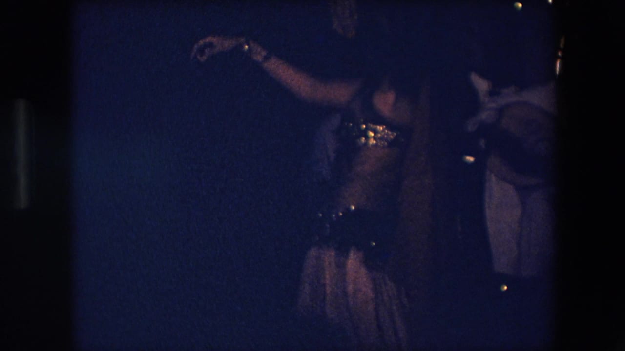 Dancer in an embellished costume performs in dim blue light near musicians.