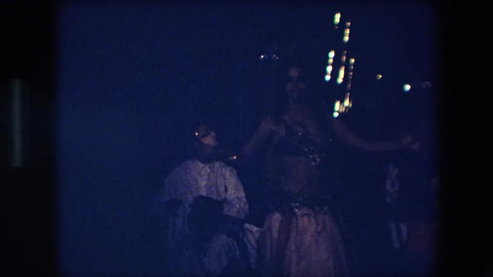 In Algeria in 1971, a female dancer appears in an ornate costume under low blue light while a seated audience member watches in the foreground.