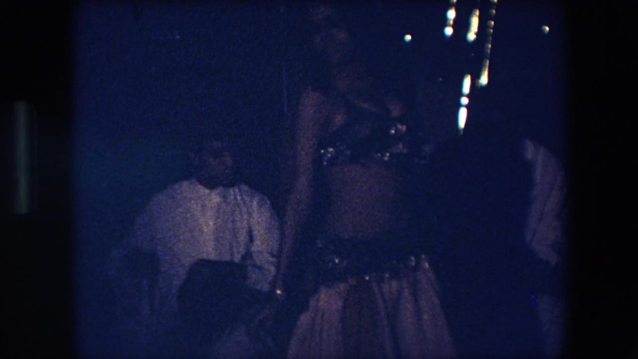 Dancer standing near seated viewers in a dark indoor performance space.