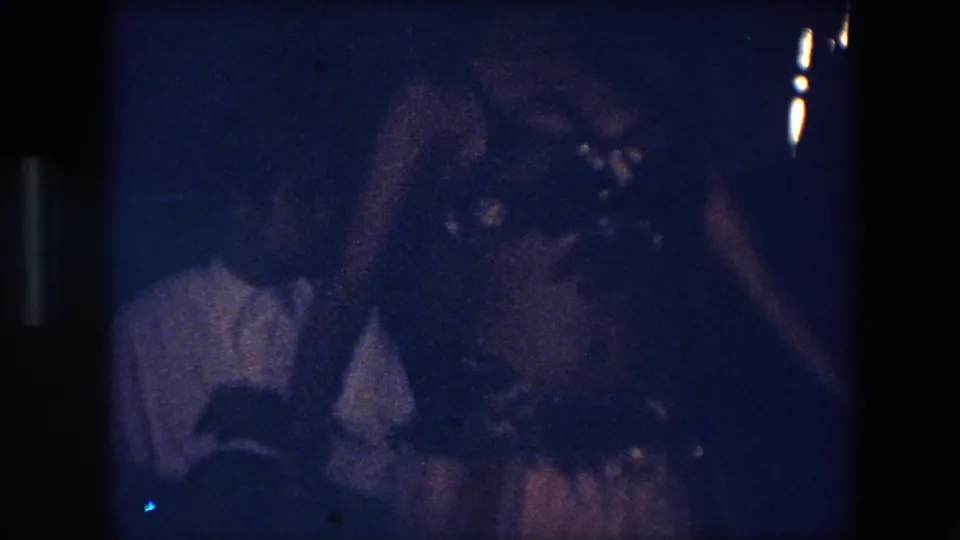 In the final frame, the dancer is close to the camera with her ornate top and belt visible, while a seated viewer in a light shirt appears behind her in the dark room.