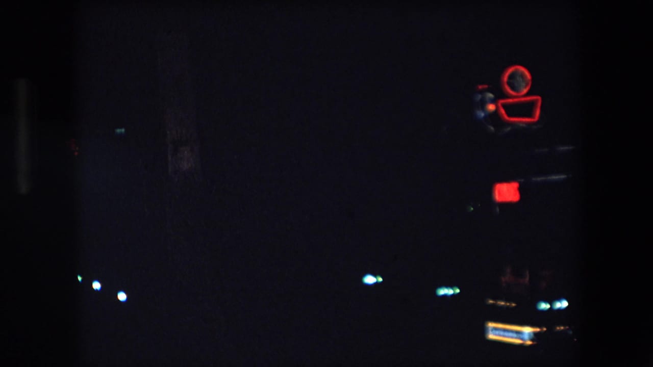Red neon camera-shaped sign at upper right with dim city lights across a dark frame.
