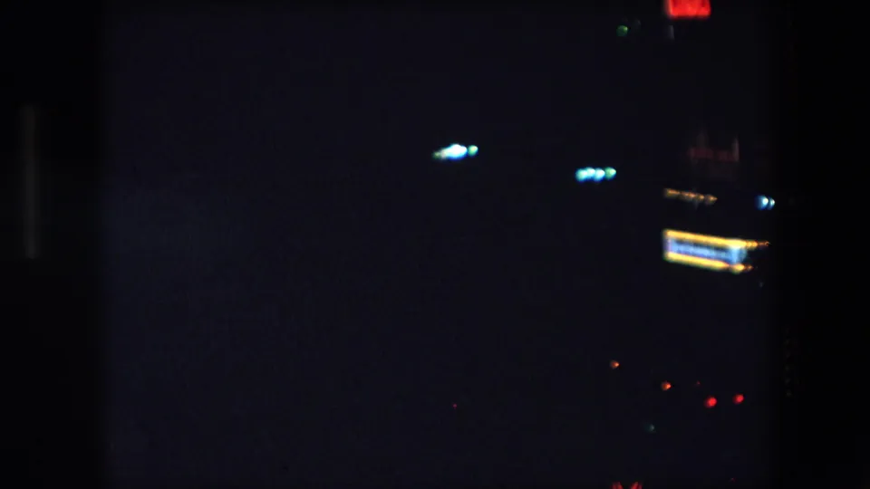 1971 Barcelona 8mm night frame with the red neon sign partly cropped at right, small blue-white lights, and deep underexposed urban darkness.