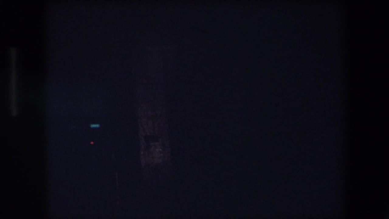 Low-light 8mm frame from a nighttime drive in Barcelona, showing small bright light points and indistinct vertical city forms.