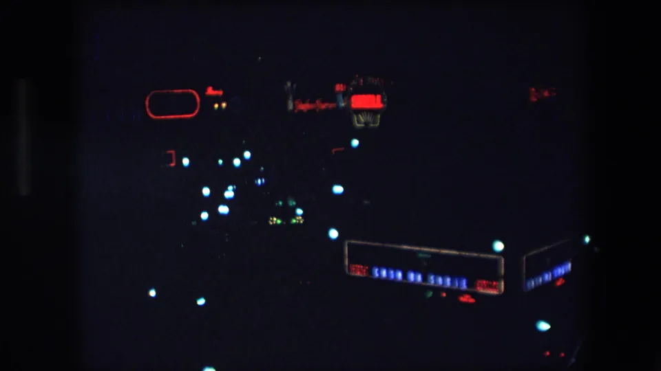Dark 1971 Barcelona 8mm frame showing red illuminated lettering or signage with clusters of blue-white lights and a rectangular lighted display near the lower right.