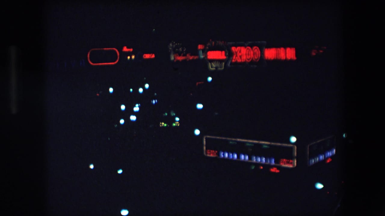 1971 Barcelona home-movie frame showing a dark night view with a red Shell X100 Motor Oil sign and distant colored city lights.