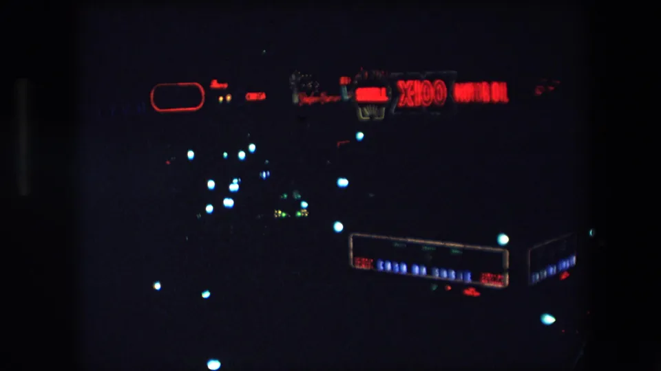 1971 Barcelona home-movie frame showing a dark night view with a red Shell X100 Motor Oil sign and distant colored city lights.