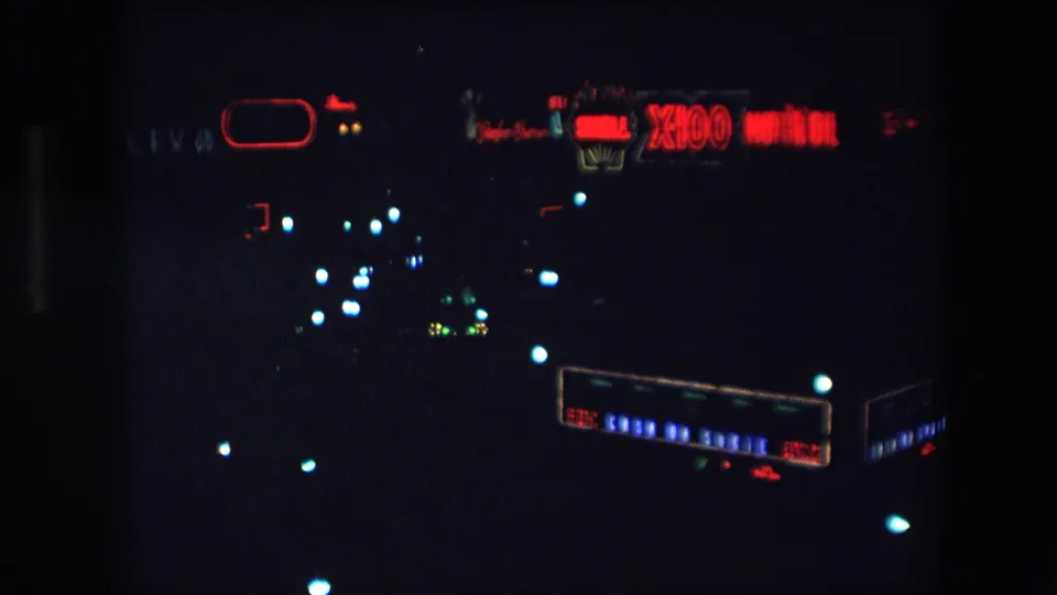 1971 Barcelona nighttime frame with a red Shell X100 Motor Oil sign, dark skyline, and soft blue-white points of city light.