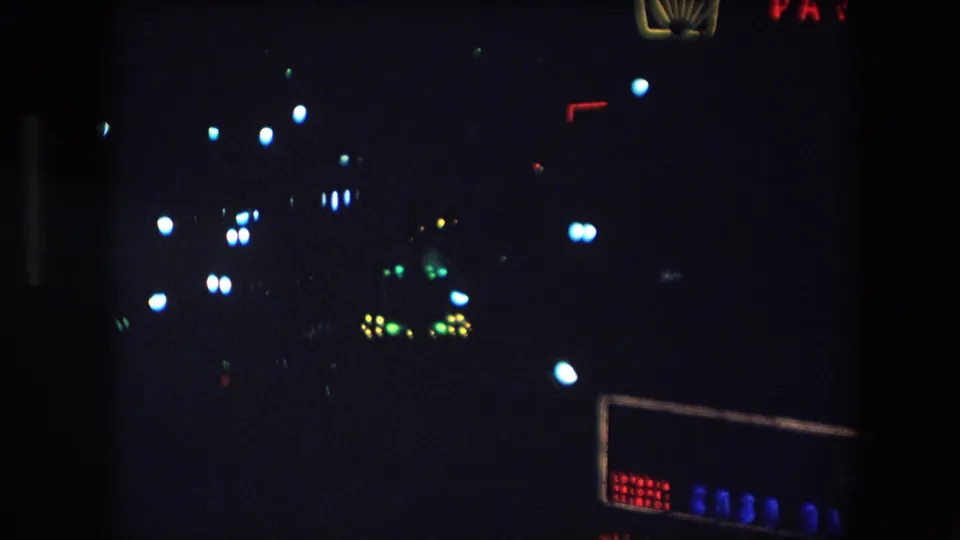 1971 Barcelona home-movie frame with partial red neon signage, a Shell emblem near the upper edge, and a lower row of blue lights in deep shadow.