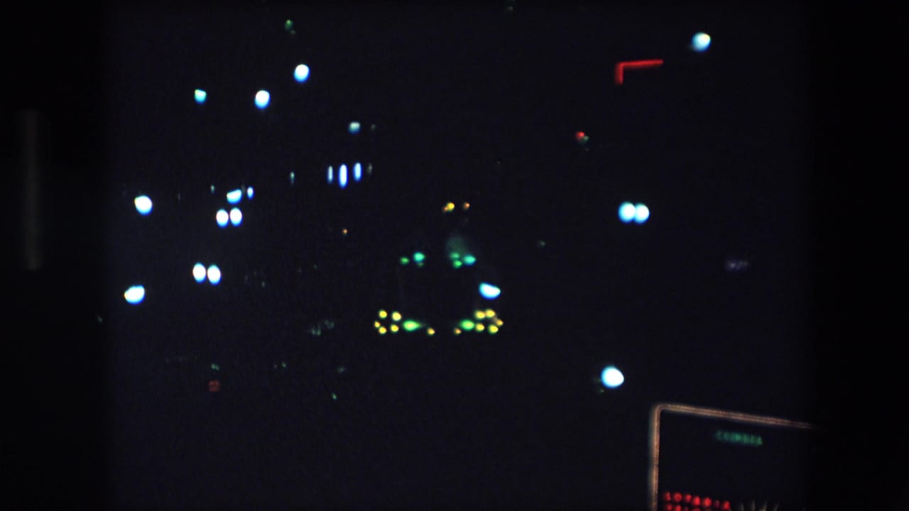 1971 Barcelona home-movie frame showing distant white, green, yellow, and red lights against a very dark nighttime view.