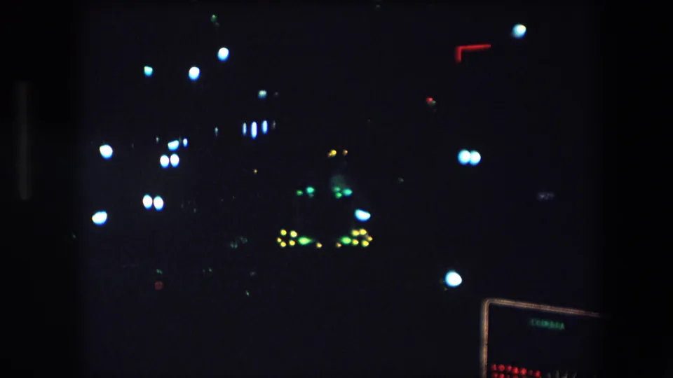 1971 Barcelona home-movie frame showing distant white, green, yellow, and red lights against a very dark nighttime view.
