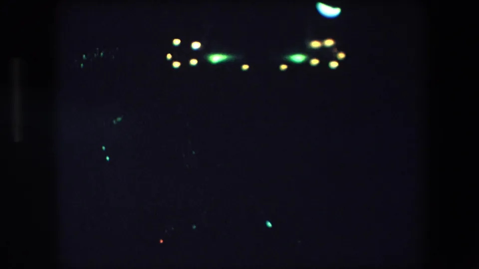 1971 Barcelona 8mm frame with distant green and yellow light clusters near the top of a mostly dark, grainy night scene.