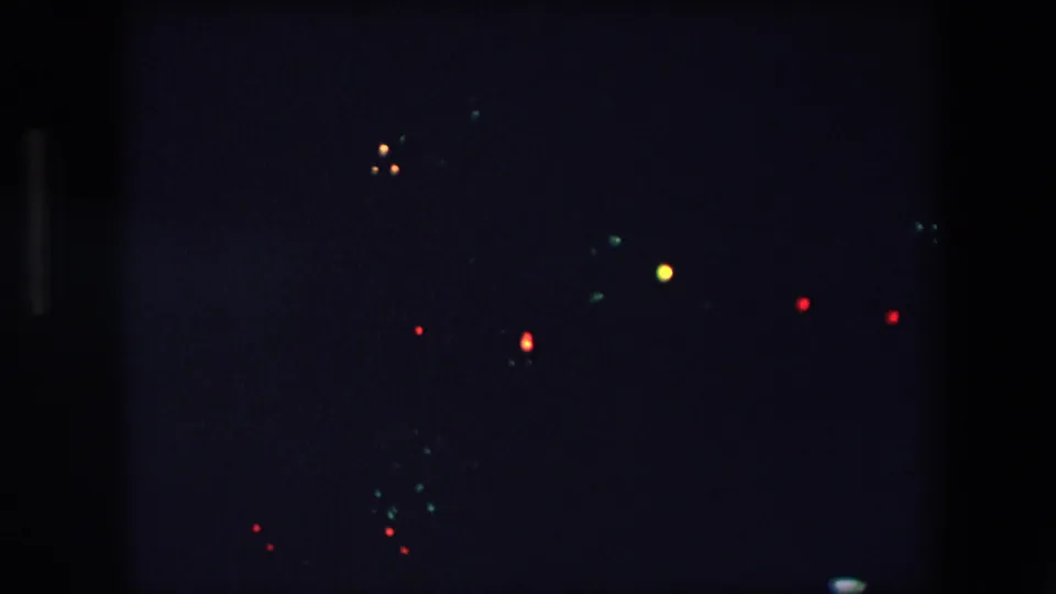 1971 Barcelona 8mm frame showing scattered red, green, blue, and yellow points of light in a heavily underexposed night view.